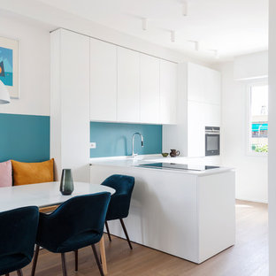 Foto di una cucina minimal di medie dimensioni con lavello integrato, ante lisce, ante bianche, top in superficie solida, paraspruzzi blu, elettrodomestici neri, pavimento in legno massello medio, penisola, top bianco e pavimento marrone
