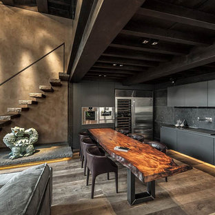 Idee per una cucina ad ambiente unico industriale con ante lisce, ante nere, paraspruzzi nero, elettrodomestici in acciaio inossidabile, pavimento marrone e top nero
