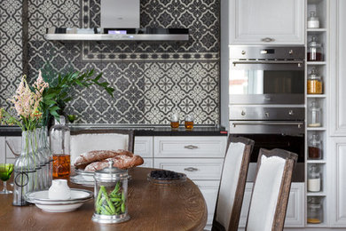 Modelo de cocina comedor clásica de tamaño medio con electrodomésticos de acero inoxidable, suelo de baldosas de porcelana, suelo beige, encimeras negras, salpicadero verde y con blanco y negro