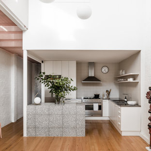 Inspiration for an industrial l-shaped eat-in kitchen in Melbourne with flat-panel cabinets, white cabinets, stainless steel benchtops, white splashback, stainless steel appliances, medium hardwood floors, a peninsula and brown floor.