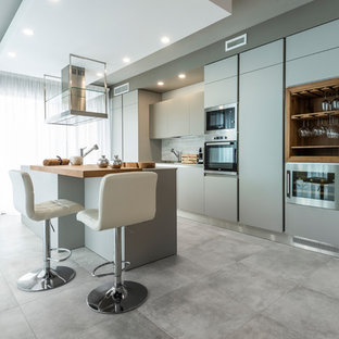 Foto de cocina de galera, ecléctica, con suelo de baldosas de porcelana, suelo gris, armarios con paneles lisos, puertas de armario grises, encimera de madera, salpicadero verde, electrodomésticos con paneles, una isla y encimeras marrones