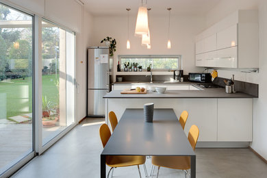 Идея дизайна: п-образная кухня среднего размера в современном стиле с обеденным столом, плоскими фасадами, белыми фасадами, техникой из нержавеющей стали, бетонным полом, полуостровом, серым полом, врезной мойкой и мойкой у окна