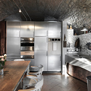 Immagine di una cucina a L industriale con lavello a doppia vasca, ante in acciaio inossidabile, ante lisce, paraspruzzi con piastrelle a mosaico, elettrodomestici in acciaio inossidabile, pavimento in mattoni, nessuna isola, pavimento marrone e top grigio