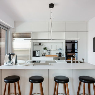 Idee per un grande cucina con isola centrale con ante lisce, paraspruzzi bianco, elettrodomestici in acciaio inossidabile, top bianco, lavello sottopiano, ante bianche e pavimento in legno massello medio