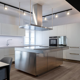 Ispirazione per una grande cucina minimal con lavello sottopiano, ante lisce, ante bianche, paraspruzzi bianco, parquet chiaro, top in acciaio inossidabile, elettrodomestici da incasso, pavimento marrone e top grigio
