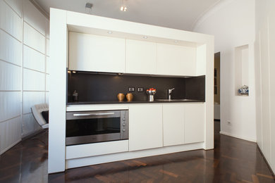 ローマにある高級な中くらいなコンテンポラリースタイルのおしゃれなキッチン (ドロップインシンク、フラットパネル扉のキャビネット、白いキャビネット、御影石カウンター、黒いキッチンパネル、大理石のキッチンパネル、シルバーの調理設備、濃色無垢フローリング、茶色い床、黒いキッチンカウンター) の写真