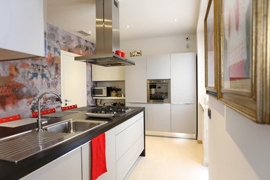 Immagine di una cucina abitabile minimal di medie dimensioni con lavello da incasso, ante lisce, ante grigie, elettrodomestici in acciaio inossidabile e penisola