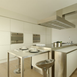 Foto di una cucina minimalista con lavello sottopiano, ante lisce, ante bianche, top in acciaio inossidabile, parquet chiaro, pavimento beige e top grigio
