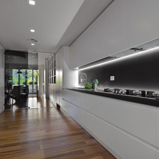 Ispirazione per una grande cucina lineare design con lavello da incasso, ante lisce, ante bianche, paraspruzzi nero, elettrodomestici da incasso, nessuna isola, pavimento marrone e top nero