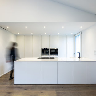 Esempio di una cucina parallela minimalista con isola, top bianco, ante lisce, ante bianche, elettrodomestici in acciaio inossidabile, parquet scuro e pavimento marrone