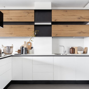 Idee per una cucina a L contemporanea di medie dimensioni con lavello sottopiano, ante lisce, ante bianche, paraspruzzi bianco, pavimento in cemento, penisola, pavimento grigio e top bianco