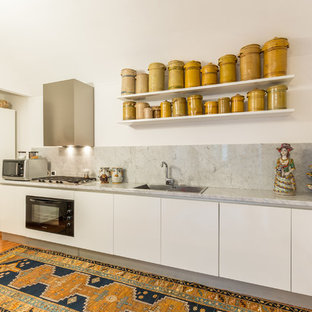 Ispirazione per una cucina lineare mediterranea con lavello da incasso, ante lisce, ante bianche, top in marmo, paraspruzzi grigio, paraspruzzi in lastra di pietra, elettrodomestici neri e parquet chiaro