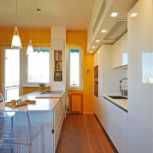 Foto di una cucina minimalista con lavello a vasca singola, ante lisce, ante bianche, paraspruzzi bianco, elettrodomestici bianchi, pavimento in laminato, penisola e top bianco