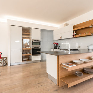 Ispirazione per una cucina ad U contemporanea con lavello da incasso, nessun'anta, ante bianche, paraspruzzi bianco, elettrodomestici in acciaio inossidabile, pavimento in legno massello medio, pavimento marrone e top grigio