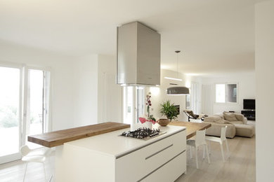 Imagen de cocina actual abierta con armarios con paneles lisos, puertas de armario blancas, suelo de madera clara y una isla