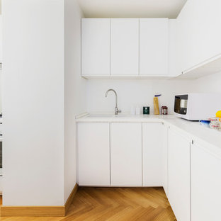 Immagine di una cucina a L contemporanea di medie dimensioni con ante lisce, ante bianche, paraspruzzi bianco, elettrodomestici bianchi, pavimento in legno massello medio, nessuna isola, pavimento marrone e top bianco