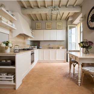 Foto di una cucina stile shabby con ante con riquadro incassato, ante bianche, elettrodomestici in acciaio inossidabile, pavimento in terracotta, nessuna isola, pavimento marrone e top beige