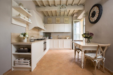 Bild på ett shabby chic-inspirerat beige beige kök, med luckor med infälld panel, vita skåp, rostfria vitvaror, klinkergolv i terrakotta och brunt golv