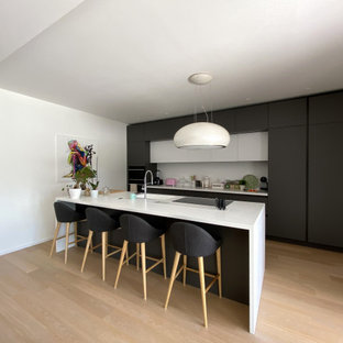 Ispirazione per una grande cucina contemporanea con lavello integrato, ante lisce, ante nere, top in superficie solida, paraspruzzi bianco, elettrodomestici neri, parquet chiaro e top bianco