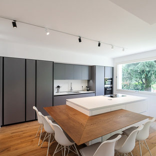 Immagine di una cucina design con lavello sottopiano, ante lisce, ante grigie, paraspruzzi bianco, elettrodomestici neri, parquet chiaro, isola e top bianco