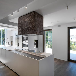 Foto di una cucina minimalista con ante lisce, ante bianche, lavello integrato, elettrodomestici in acciaio inossidabile, pavimento in legno massello medio, pavimento marrone e top bianco