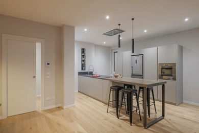 Exempel på ett stort modernt kök med öppen planlösning, med en undermonterad diskho, grå skåp, bänkskiva i kvartsit, rostfria vitvaror, ljust trägolv och en halv köksö
