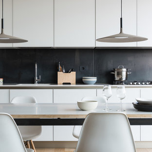 Photo of a modern single-wall eat-in kitchen in Rome with an integrated sink, flat-panel cabinets, white cabinets, quartzite benchtops, black splashback, slate splashback, white appliances, light hardwood floors and white benchtop.