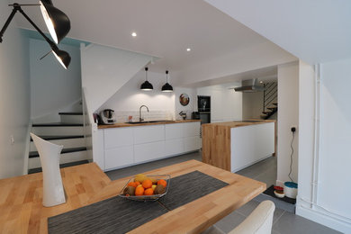 Bild på ett stort funkis brun linjärt brunt kök och matrum, med vita skåp, träbänkskiva, en köksö, en undermonterad diskho, vitt stänkskydd, integrerade vitvaror och grått golv