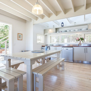 Idées déco pour une cuisine américaine exotique en L avec un placard à porte plane, des portes de placard beiges, un plan de travail en bois, une crédence métallisée, un électroménager en acier inoxydable, un sol en bois clair, un sol beige et un plan de travail marron.