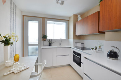 Modern inredning av ett avskilt, litet vit linjärt vitt kök, med en enkel diskho, släta luckor, vita skåp, vitt stänkskydd, klinkergolv i keramik och beiget golv