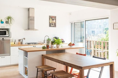 Modelo de cocina comedor contemporánea grande con fregadero encastrado, puertas de armario blancas, encimera de madera, electrodomésticos de acero inoxidable, suelo de madera clara, una isla, armarios con paneles lisos, salpicadero blanco, suelo marrón y encimeras marrones