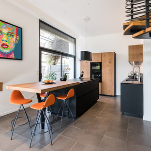 Idées déco pour une cuisine contemporaine en L avec un évier encastré, un placard à porte plane, des portes de placard en bois brun, un électroménager noir, un îlot central, un sol gris et un plan de travail noir.