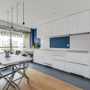 Exemple d'une grand cuisine américaine linéaire tendance avec un placard à porte plane, des portes de placard blanches, une crédence bleue, un sol en bois clair et un évier encastré.