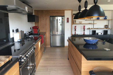 Photo of a large contemporary l-shaped kitchen/diner in Nice with a submerged sink, beaded cabinets, medium wood cabinets, granite worktops, black splashback, black appliances, light hardwood flooring, an island and beige floors.