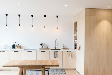 Diseño de cocina comedor nórdica con fregadero de un seno, armarios con paneles lisos, puertas de armario de madera clara, suelo de madera clara y encimeras blancas
