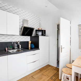Inspiration pour une petit cuisine américaine linéaire nordique avec des portes de placard blanches, un plan de travail en stratifié, une crédence noire, aucun îlot, un plan de travail noir, un évier posé, un placard à porte plane, un sol en bois brun et un sol marron.