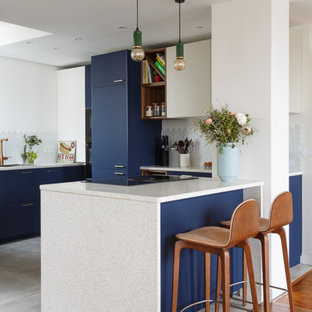 Inspiration for a large contemporary u-shaped open plan kitchen in London with a submerged sink, flat-panel cabinets, blue cabinets, granite worktops, white splashback, porcelain splashback, integrated appliances, ceramic flooring, a breakfast bar, grey floors and white worktops.