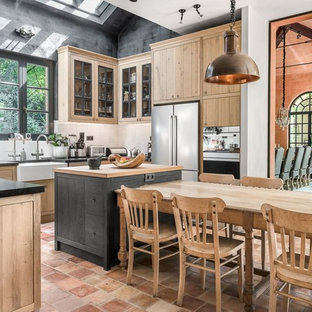 Inspiration for a farmhouse u-shaped kitchen/diner in Marseille with a belfast sink, glass-front cabinets, light wood cabinets, white splashback, stainless steel appliances, terracotta flooring, an island and orange floors.