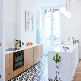 Design ideas for a mid-sized contemporary galley open plan kitchen in Lyon with an integrated sink, light wood cabinets, white splashback, black appliances, cement tiles, with island and multi-coloured floor.