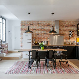 Inspiration pour une grand cuisine américaine urbaine en L avec un évier posé, des portes de placard noires, une crédence métallisée, une crédence en dalle métallique, un électroménager en acier inoxydable, un sol en bois clair et aucun îlot.