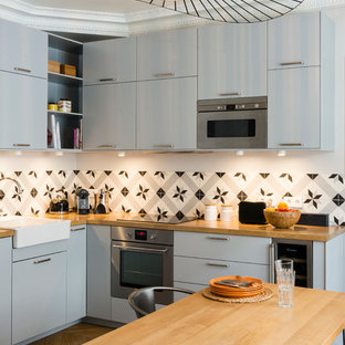 Idée de décoration pour une cuisine américaine design en L de taille moyenne avec un placard à porte plane et des portes de placard grises.