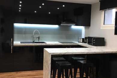Immagine di una cucina moderna di medie dimensioni con lavello integrato, ante nere, top in laminato, paraspruzzi grigio, paraspruzzi con lastra di vetro, elettrodomestici da incasso e pavimento in laminato