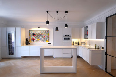 パリにある高級な広いコンテンポラリースタイルのおしゃれなキッチン (一体型シンク、白いキャビネット、大理石カウンター、白い調理設備、淡色無垢フローリング、ベージュの床、白いキッチンカウンター) の写真