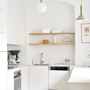 Idées déco pour une cuisine ouverte contemporaine en U de taille moyenne avec un évier intégré, des portes de placard blanches, un plan de travail en surface solide, une crédence blanche, un électroménager encastrable, un sol en bois clair et un plan de travail blanc.