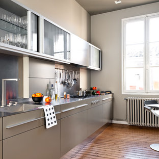Aménagement d'une cuisine parallèle contemporaine fermée et de taille moyenne avec un évier intégré, un placard à porte plane, des portes de placard grises, un plan de travail en inox, une crédence métallisée, un sol en bois brun et aucun îlot.
