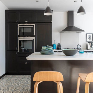 Inspiration pour une cuisine ouverte design en L de taille moyenne avec des portes de placard noires, un plan de travail en surface solide, un sol en carrelage de céramique, un îlot central, une crédence blanche, un évier encastré, un électroménager encastrable et un sol multicolore.