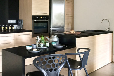 Exemple d'une petite cuisine ouverte parallèle tendance en bois clair avec un évier encastré, un placard à porte affleurante, un plan de travail en stratifié, une crédence noire, un électroménager en acier inoxydable et îlot.