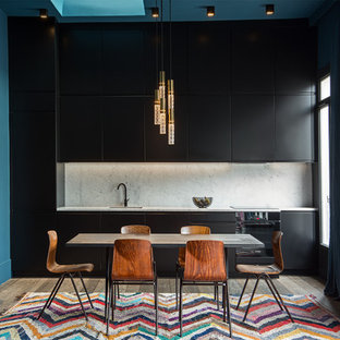 Réalisation d'une cuisine américaine linéaire design de taille moyenne avec un placard à porte affleurante, des portes de placard noires, un plan de travail en marbre, une crédence en marbre, un évier encastré, une crédence blanche, un électroménager noir, un sol en bois brun, un îlot central et un sol marron.