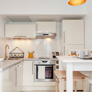 Idée de décoration pour une petit cuisine américaine design en L avec un placard à porte plane, des portes de placard blanches, une crédence blanche, une crédence en carreau de céramique et un électroménager encastrable.