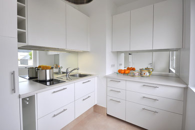 Modelo de cocinas en L minimalista pequeña con fregadero integrado, armarios con paneles lisos, puertas de armario blancas y salpicadero con efecto espejo